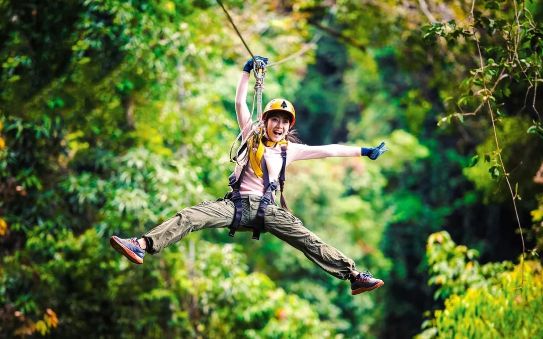 Adventurer strapped into safety harness gliding across tree canopy zip line