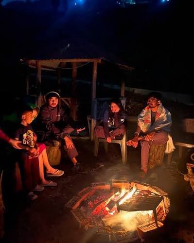 Guests seated on rustic logs around glowing campfire at night