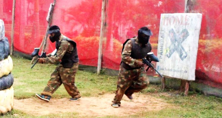 Teams in safety gear playing tactical paintball between obstacles